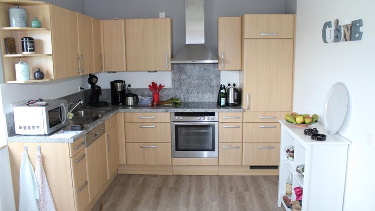 Une cuisine moderne avec des armoires en bois et des murs gris. L'équipement comprend un micro-ondes, une cuisinière et des fruits frais sur le plan de travail.