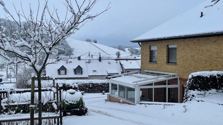 Ein verschneites Dorf mit weißen Häusern und einem klaren, grauen Himmel. Die Landschaft ist ruhig und winterlich, mit schneebedeckten Dächern und Bäumen.