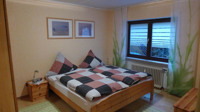 A cozy bedroom with a double bed and checkered bedspreads. Light filters through the window, and there are some decorative plant motifs on the wall.