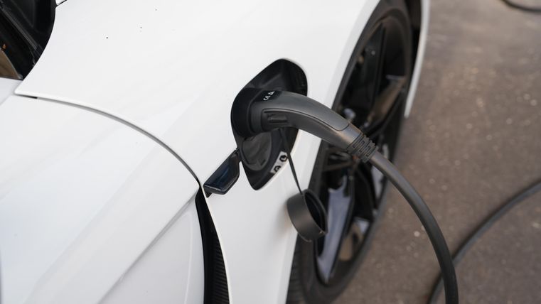 Een witte elektrische auto die wordt opgeladen bij een oplaadpunt. De laadsnoer is in de voertuigopening gestoken.