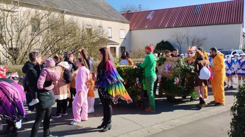 Eine Gruppe von Menschen in bunten Kostümen versammelt sich auf einer Straße. Es scheint eine fröhliche Feier oder einen Umzug zu geben.