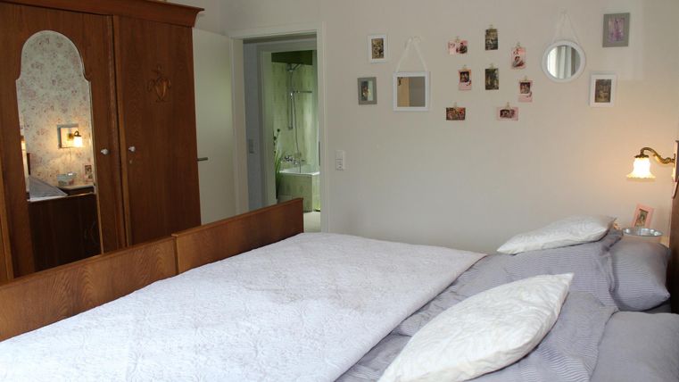 Une chambre confortable avec un grand lit et une commode en bois. Différentes images sont accrochées au mur, et un miroir reflète la lumière.