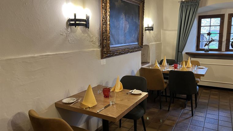 Ein gemütliches Restaurant mit Holztischen und eleganten Platzdecken. An der Wand hängt ein großes Gemälde, und durch das Fenster fällt sanftes Licht.