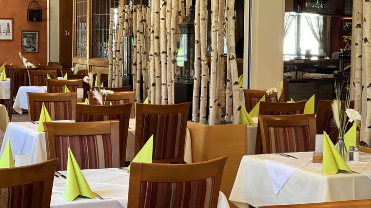 A modern restaurant with elegant tables and wooden decorations. Green napkins and birch logs create an inviting atmosphere.