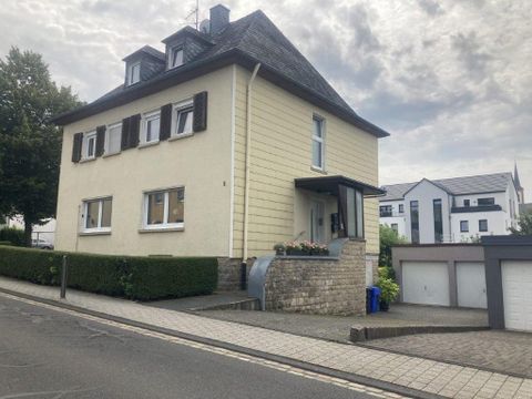 Ein zweigeschossiges Haus mit hellgelber Fassade und dunklem Dach. Es befindet sich an einer ruhigen Straße mit einigen Nachbargebäuden.