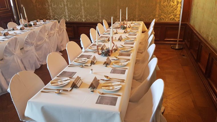 An elegantly set table in a festive room. The tables are decorated with white tablecloths, cutlery, and candles.