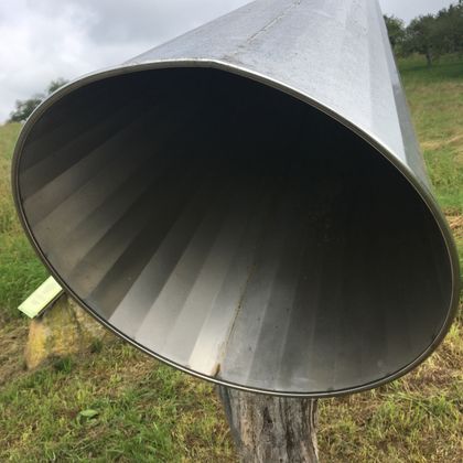 Großes Metallhörrohr auf einer Wiese, das auf einem Holzstumpf montiert ist.