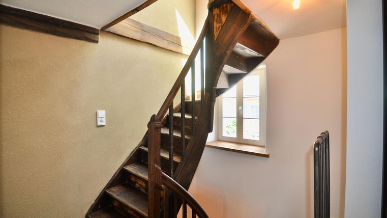 A beautiful wooden spiral staircase in a bright room. The window allows for plenty of daylight.