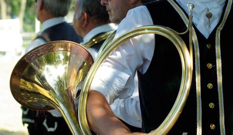 Eine Gruppe von Musikern in traditionellen Anzügen hält ein serträtes Blasinstrument. Der Fokus liegt auf einem glänzenden Horn in der Hand eines der Musiker.