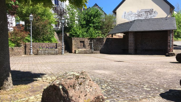 Dorfplatz in Gransdorf mit Steinmauer, Laternen und bemalter Hauswand.