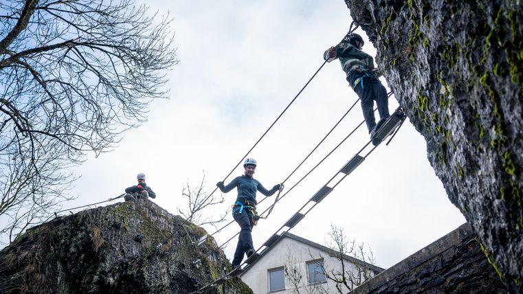 Two climbers cross a suspension bridge between two rocks.