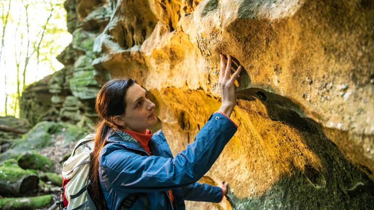 Eine Frau berührt einen Felsen in einem Wald.
