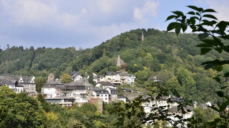Blick auf die Stadt Kyllburg mit Häusern und einer Kirche, umgeben von bewaldeten Hügeln.