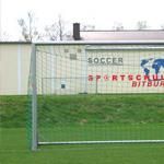 Ein Fußballtor auf einem grünen Spielfeld. Im Hintergrund ist ein Gebäude mit dem Schriftzug „Sportschule Bitburg“ zu sehen.