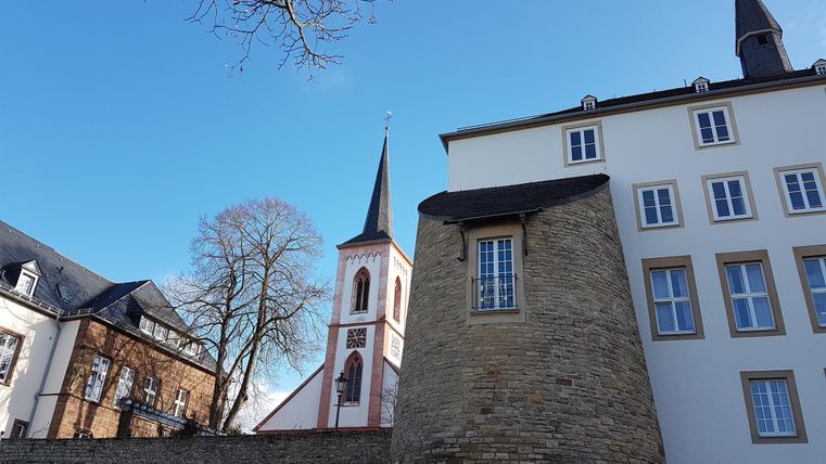 Ein Blick auf historische Gebäude mit einem Kirchturm im Hintergrund. Der Himmel ist klar und blau.