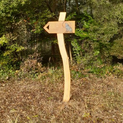 Holzwegweiser mit Wolfssymbol im Wald.