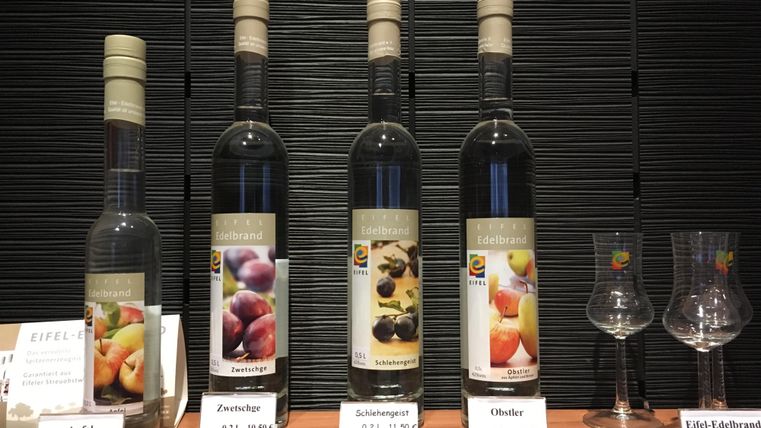 Vier flessen met verschillende fruitschnaps zijn op een tafel gepresenteerd. Naast de flessen staan twee glazen en prijskaartjes voor de producten.