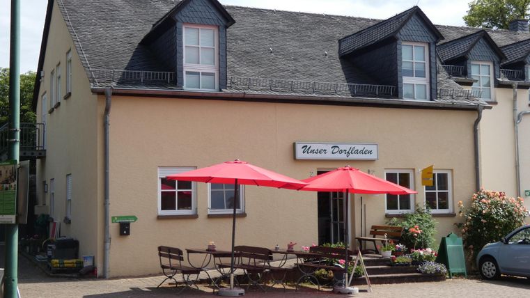 A cozy building with a sign above the entrance.
In front of the house, there are tables and sun loungers, shaded by red parasols.