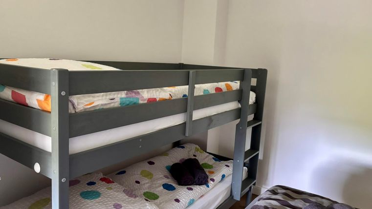 Une chambre d'enfant avec un lit superposé et un lit simple. La literie a des motifs colorés sur fond blanc.