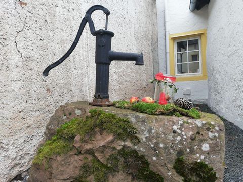 An old-fashioned water pump stands on a moss-covered stone. Next to it lie some apples and a pine cone.