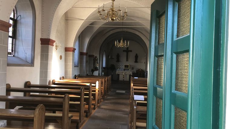Vue intérieure d'une petite chapelle avec des bancs en bois et un autel en arrière-plan.