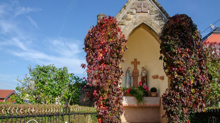 Eine kleine Kapelle mit Statuen und herbstlichem Efeu bewachsen.