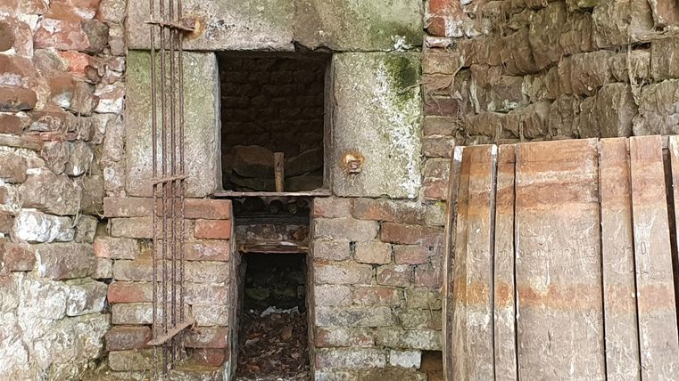 An old, brick structure with open gates. Next to it, some wooden planks lie on the ground.