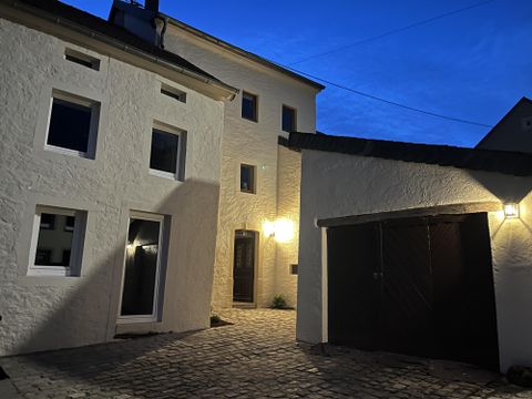 Een rustige binnenplaats met witte huizen en een garagepoort. De scène is bij schemerlicht met een warme buitenverlichting.