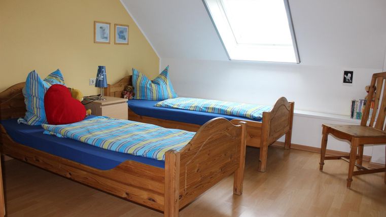 Ein gemütliches Schlafzimmer mit zwei Einzelbetten und bunten Bettwäsche. Das Zimmer hat eine helle Atmosphäre mit einem Dachfenster und einem Stuhl in der Ecke.