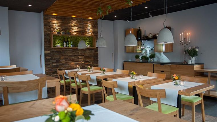 A modern restaurant with wooden tables and chairs. The decor is elegant and features greenery as well as soft lighting.