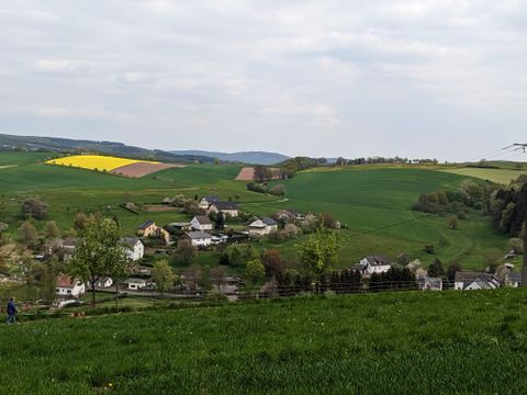 Landschaft mit grünen Feldern, gelbem Rapsfeld und Dorf im Tal.