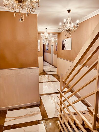 An elegant hallway with smooth, shiny tiles and a warm wall color. Ceiling lights and pictures on the walls create an inviting atmosphere.