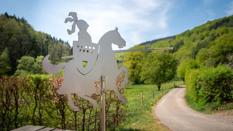 Metallfigur eines Ritters auf einem Pferd vor einer grünen Landschaft.