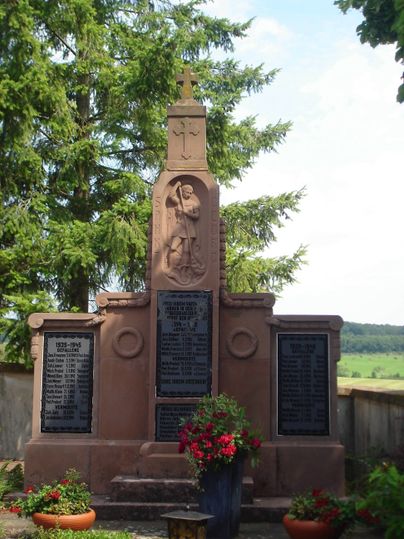 Oorlogsmonument met St George en inscripties, omringd door bomen.