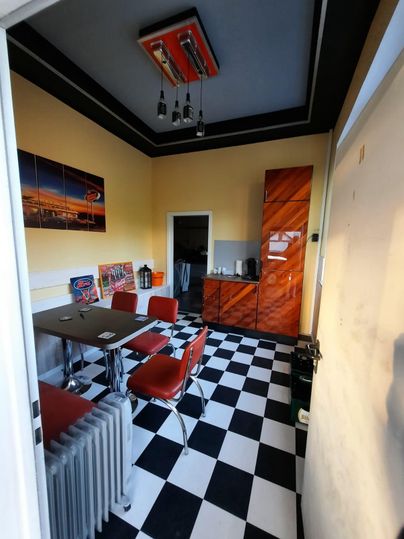 Eine gemütliche Küche mit einem schwarz-weißen Fliesenboden und rotem Mobiliar. An der Wand hängen Bilder, und es gibt einen modernen Kühlschrank sowie eine Kaffeemaschine.