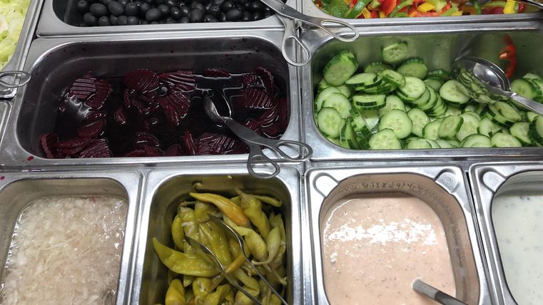 Un assortiment de légumes frais et d'accompagnements, notamment des olives, des concombres et des poivrons. Il y a aussi différentes sauces et dips dans des contenants séparés.