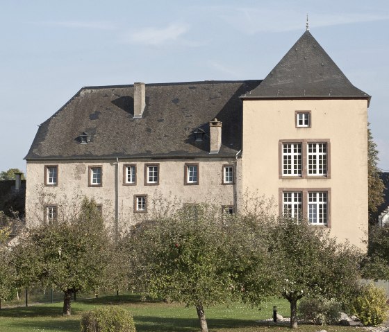 Burg Dudeldorf mit einem großen Garten voller Obstbäume im Vordergrund. Das Gebäude hat ein steiles Dach und viele Fenster., © Tourist-Info Bitburger Land