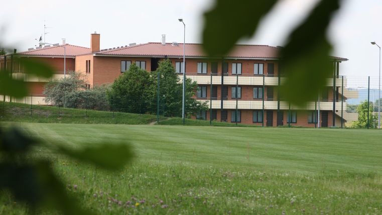 Ein modernes Gebäude mit mehreren Etagen steht in einer grünen Landschaft. Umgeben von Wiesen und Bäumen wirkt es einladend und ruhig.