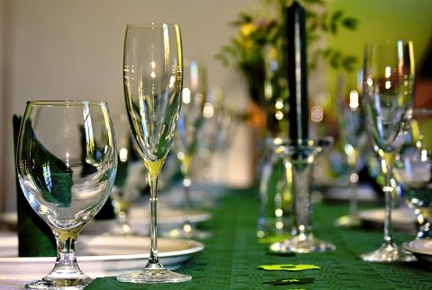A beautifully set table with glasses and candles on a green tablecloth. In the background, decorative flowers are visible.