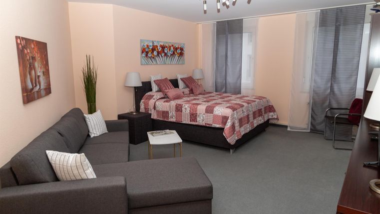 Ein gemütliches Zimmer mit einem großen Bett und einem modernen Sofa. Die Wände sind hell und es gibt Kunstbilder zur Dekoration.