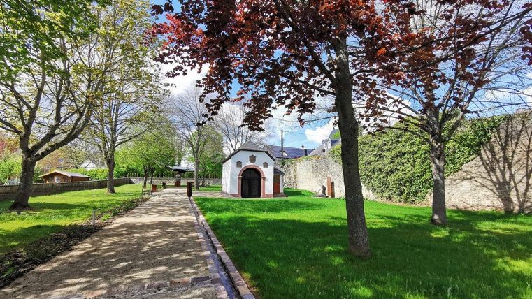 Ein kleiner weißer Pavillon in einem grünen Park mit Bäumen und einem gepflasterten Weg.