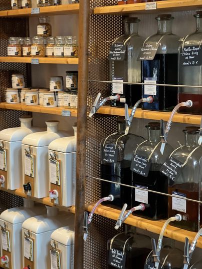 Ein gut sortierter Laden mit verschiedenen Behältern. Auf Regalen stehen Gläser und Spender mit verschiedenen Flüssigkeiten und kleinen Produkten.