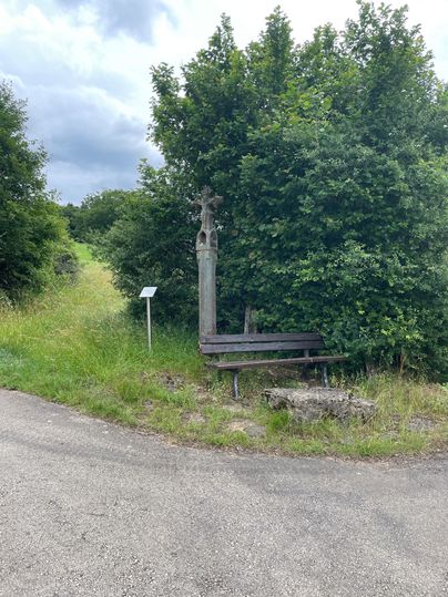 Wegekreuz und Bank am Wanderweg Oberweis, umgeben von Bäumen.