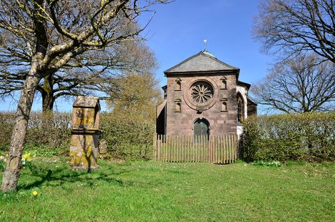 Frohnertkapelle in Oberkail mit Bäumen und einem alten Grabstein im Vordergrund.