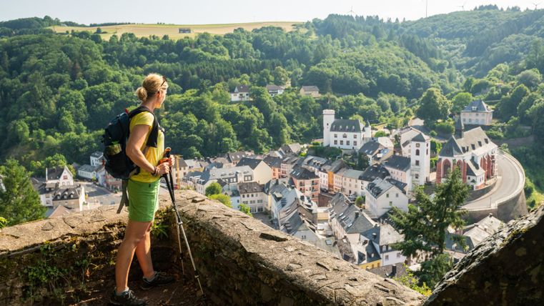 Eine Frau mit Rucksack blickt von einem Aussichtspunkt auf die Stadt Neuerburg.