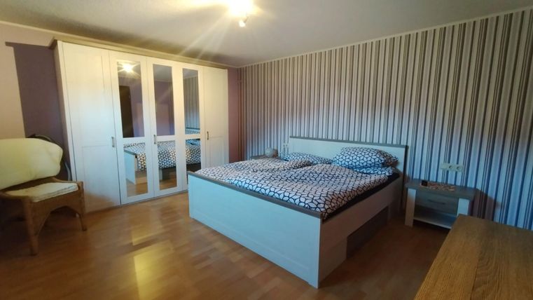 Ein gemütliches Schlafzimmer mit einem Doppelbett und gepunkteter Bettwäsche. Die Wände sind mit horizontalen Streifen dekoriert und ein großer Kleiderschrank steht im Raum.