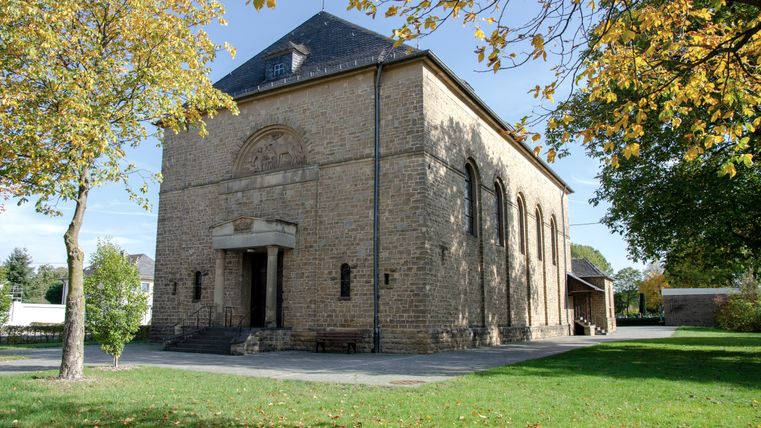 Kirche St. Hubertus in Wolsfeld, umgeben von Bäumen im Herbst.