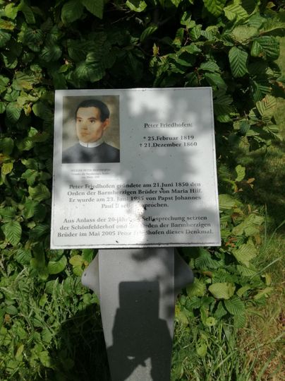 Gedenktafel für Peter Friedhofen mit Bild und Text, umgeben von grünen Blättern.