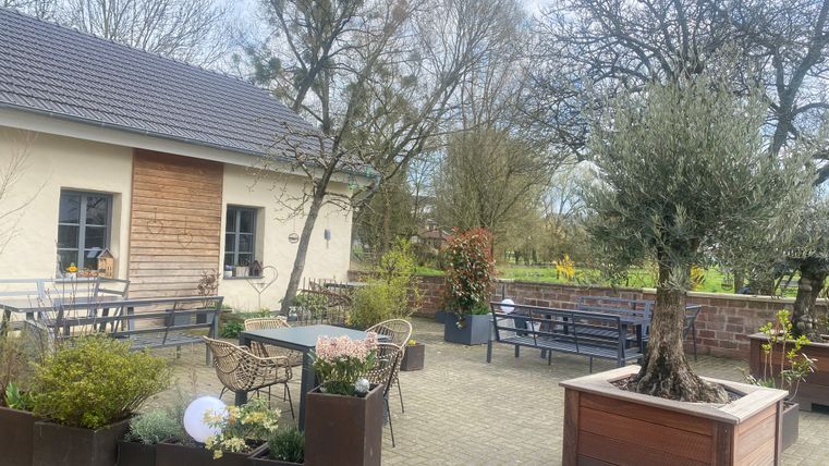 Außenbereich eines Cafés mit Tischen, Stühlen und Pflanzen.