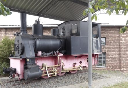 Eine alte Dampflokomotive steht unter einem Schutzdach vor einem Backsteingebäude. Die Lokomotive ist schwarz und rosa gestrichen., © Eifelverein Ortsgruppe Speicher